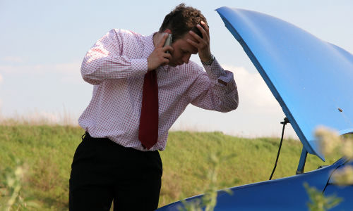 Businessman on a mobile phone in front of a broken car