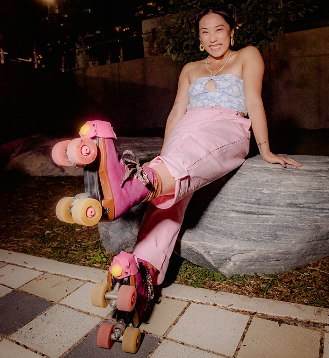 picture of a woman sitting on a rock smiling and wearing pink roller skates 
