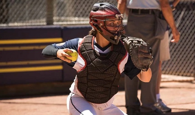 a softball catcher with a softball in her right hand and a softball mitt on her left hand