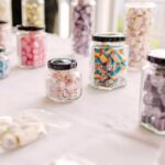 Assorted colorful candy in clear jars with black lids displayed for a candy buffet or party favors